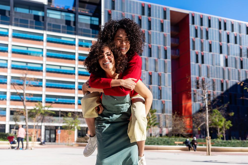 Female friends piggy backing outside on sunny day