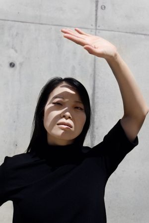 Woman blocking sunlight off her head with her hand and standing beside gray concrete wall
