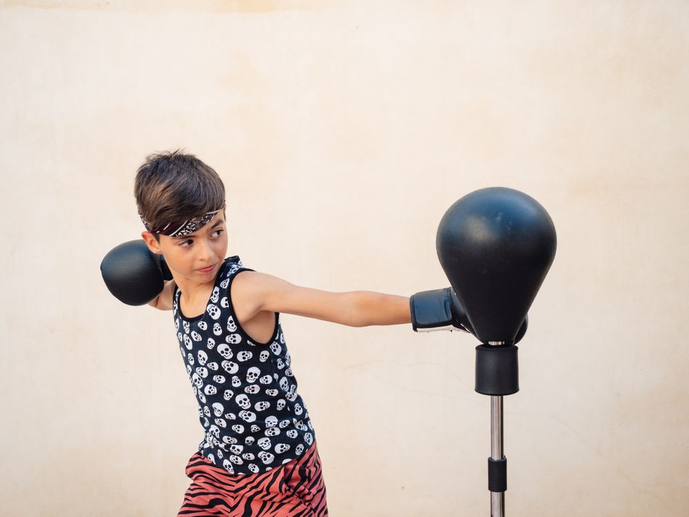 Sporty boy in boxing gloves beating punch bag