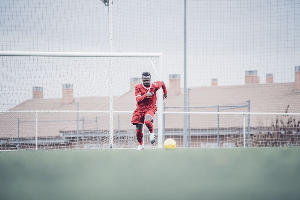 Black soccer player with red outfit playing soccer.