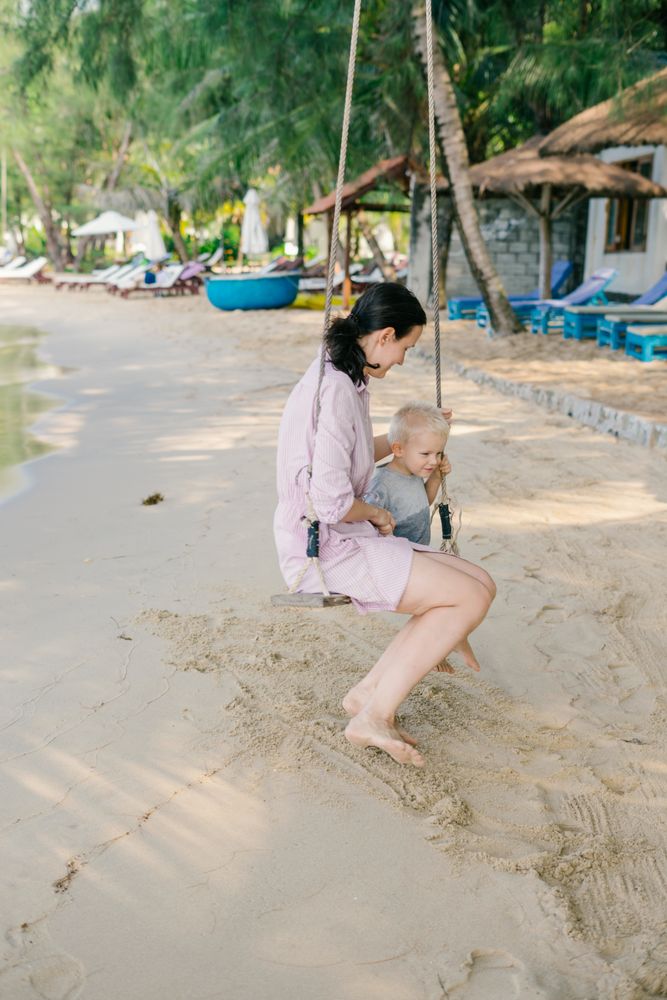 Joyful kid swinging with mother against blurred seascape