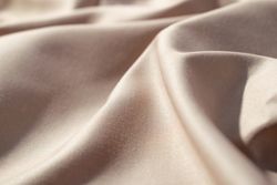 Close up silk shiny light brown fabric background texture.