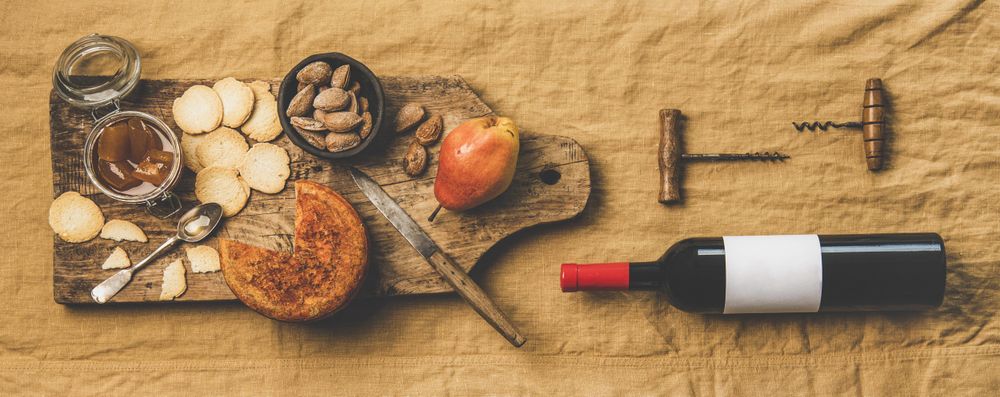 Cheese plate with bottle of red wine, cork screws on light brown linen, wide composition