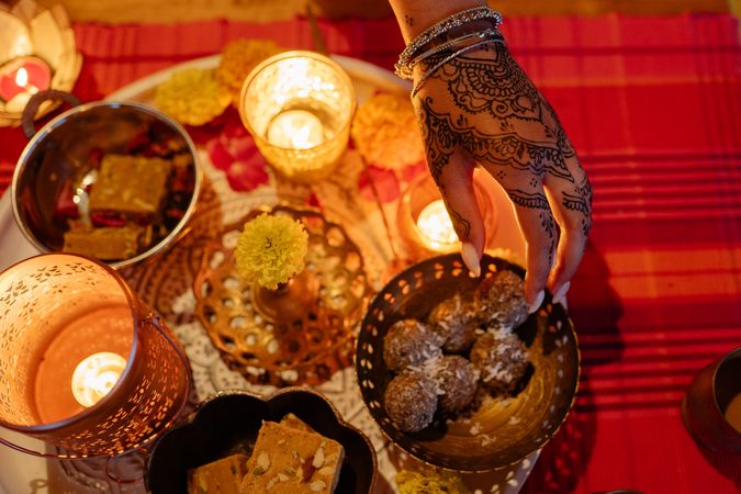 Top view of hand with mehndi beside Diwali's desserts and candles