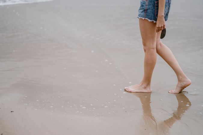 Young female walking barefoot on wet sand