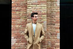 Young man standing on street with hands in camel coat pockets