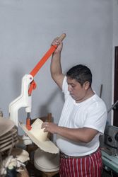 An adult Hispanic man is making a hole in a natural fiber hat