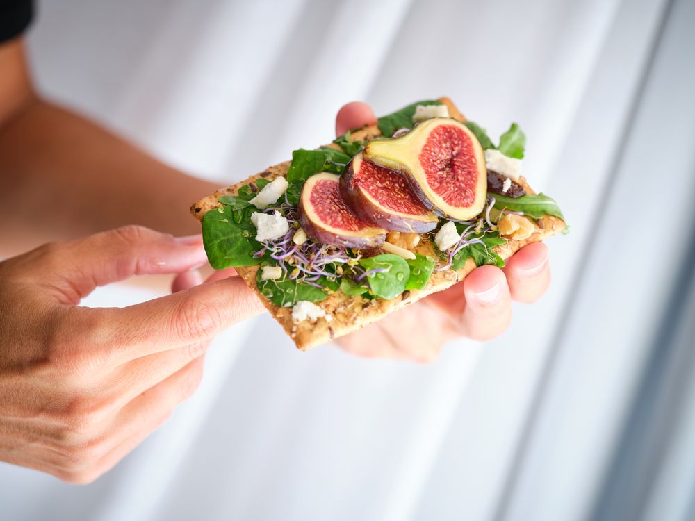 Crop person with figs on crisp bread