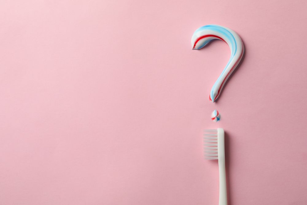 Question mark made of toothpaste and toothbrush on pink background