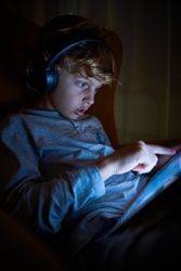Boy playing on tablet in murk room