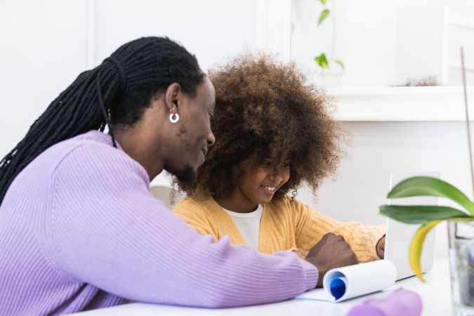 Black father helping daughter with homework on laptop