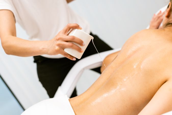 Masseuse pouring oil on back of woman awaiting a massage