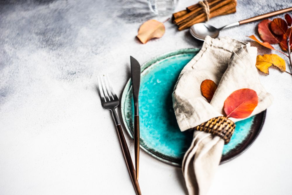 Autumn place setting with colorful leaves and cinnamon sticks garnishing teal plate with space for text