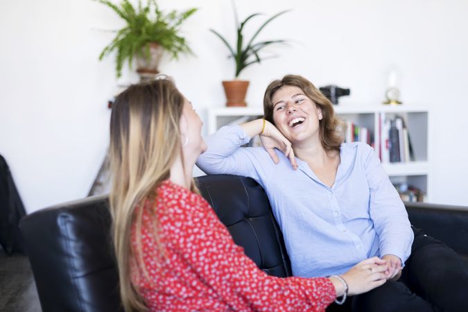 Two friends having a conversation on a sofa in the living room at home