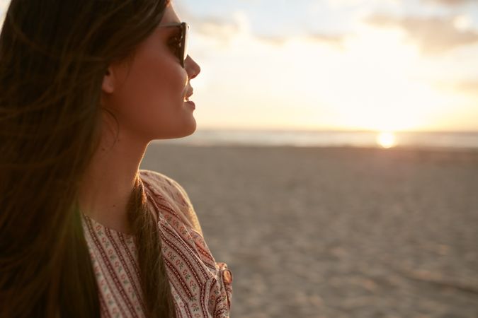Close up shot of attractive young female with sunglasses looking at sunset on the beach