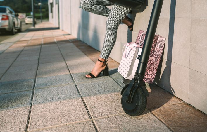 Electric scooter with shopping bags in the street and woman in background.