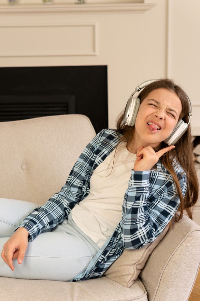 Playful girl making funny faces wearing headphones indoors.