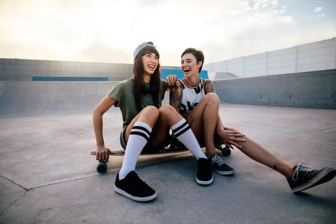 Two female friends sitting on a long board and laughing