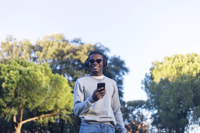 Smiling Black male with sunglasses sitting in park holding phone