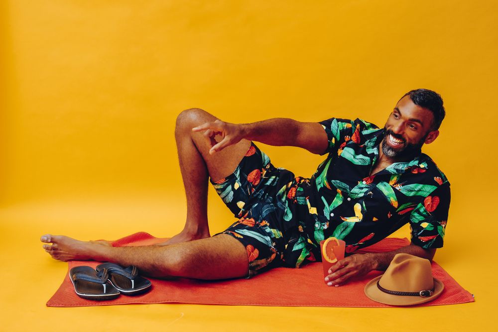 Black male laying back on towel and looking away while smiling with a tropical drink