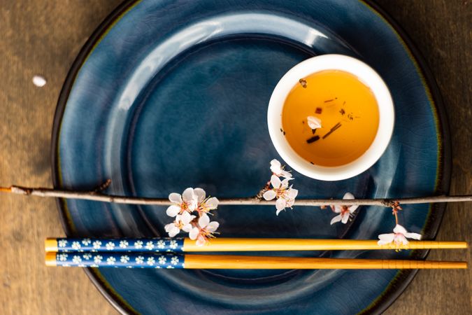 Top view of table setting with chop sticks on ceramic navy plate and decorative cherry blossom branch and cup of tea