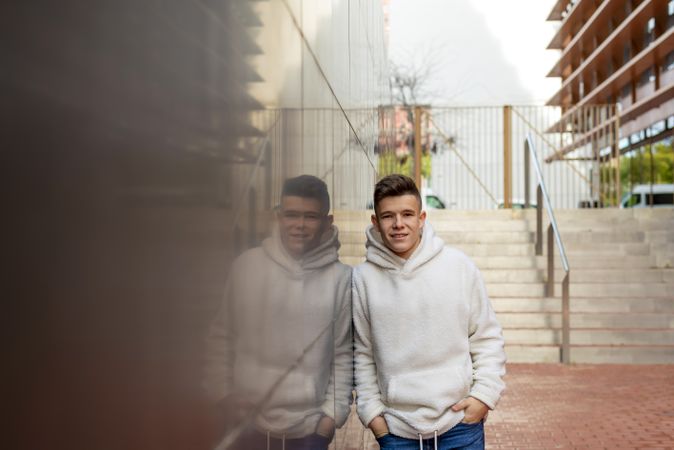 Portrait of young male with hands on pocket leaning on wall outside by staircase