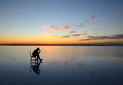 Silhouette of man sitting on chair on water