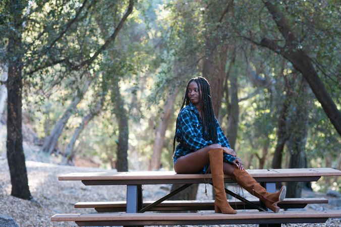 Young Black woman sitting on picnic table in the mountains in fashionable outfit
