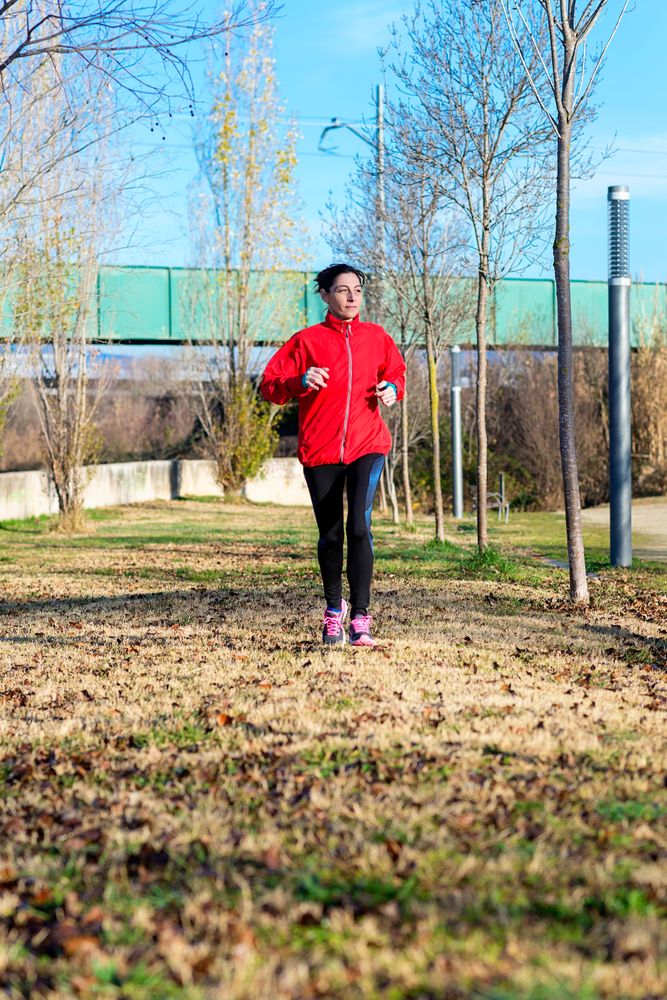Woman in red jogging outdoors in the grass on sunny fall day