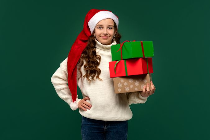 Girl in Santa hat holding stack of wrapped Christmas presents.