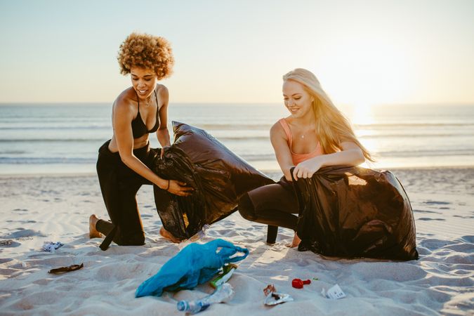 Young volunteers in surf suits gathering garbage on beach in plastic bags