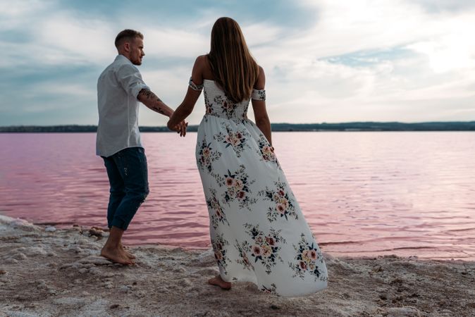 back view of adorable couple walking on an amazing beach with pink water