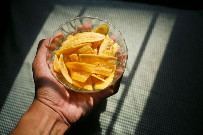 Top view of hand holding dried banana slices in bowl in morning light