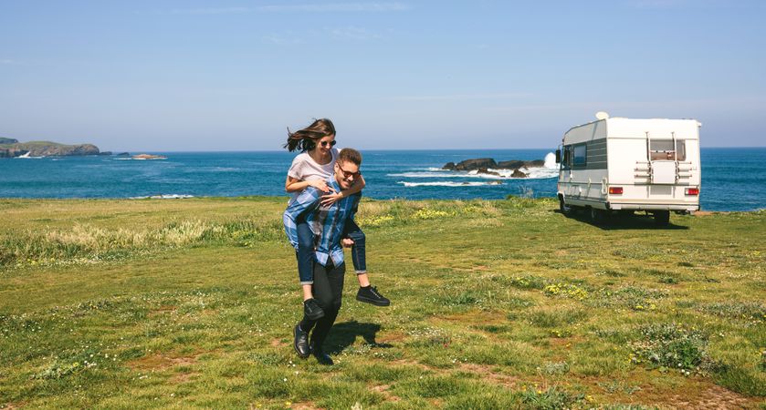 Young man piggybacking his girlfriend near the coast