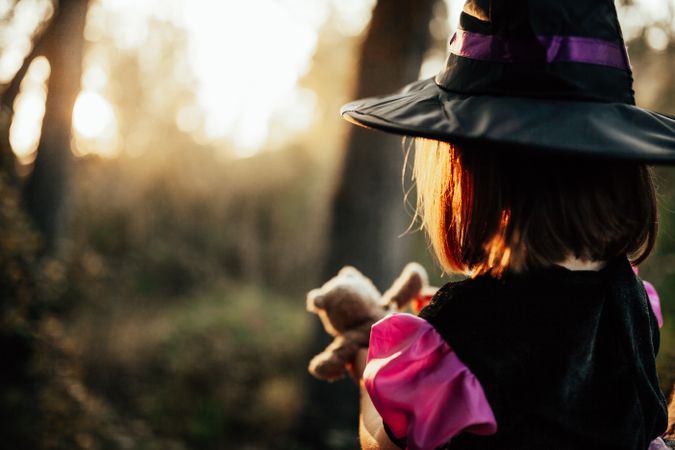 Back of girl with teddy bear in witch costume