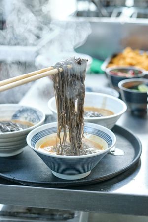 Person preparing portions of Asian noodle soup