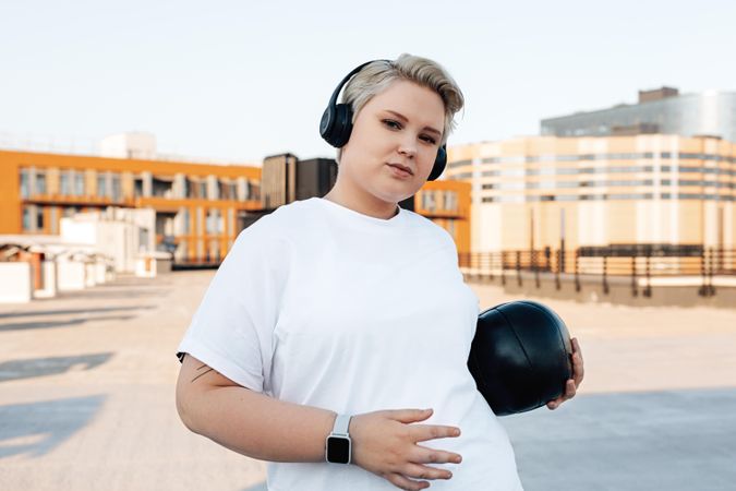 Blonde woman with medicine ball, smart watch and headphones on a rooftop