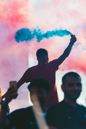 Man in red shirt holding blue smoke at a concert