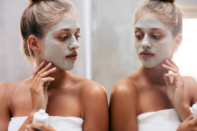 Close up shot of woman with facial mask sitting by bathroom mirror