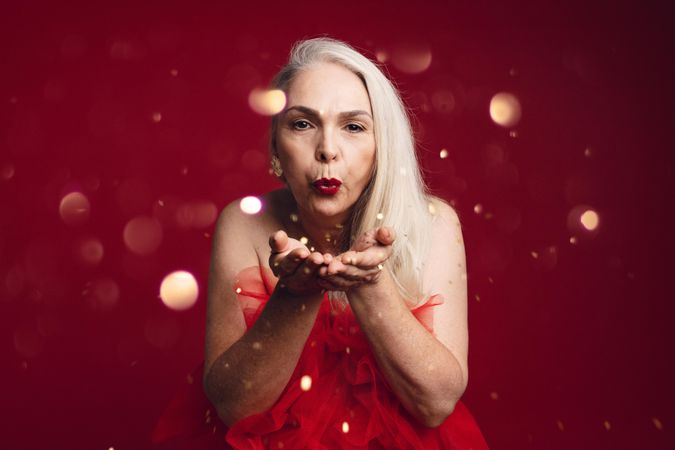 Woman blowing glitter toward camera in red dress