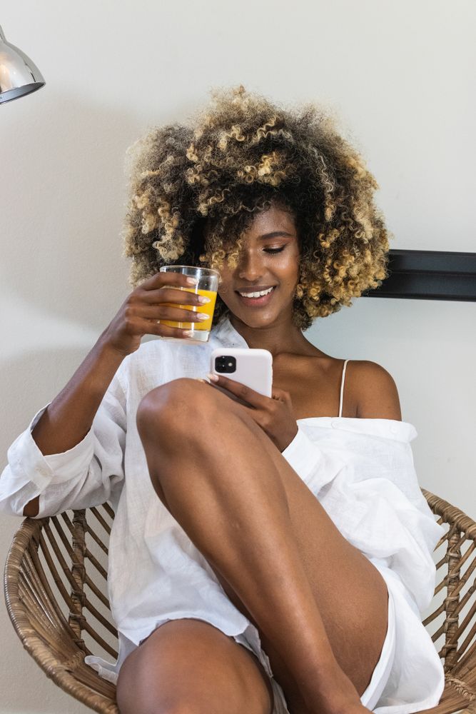 Happy Black woman sitting on armchair surfing smartphone
