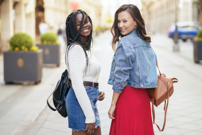 Female friends walking on a sunny outdoor street while looking back