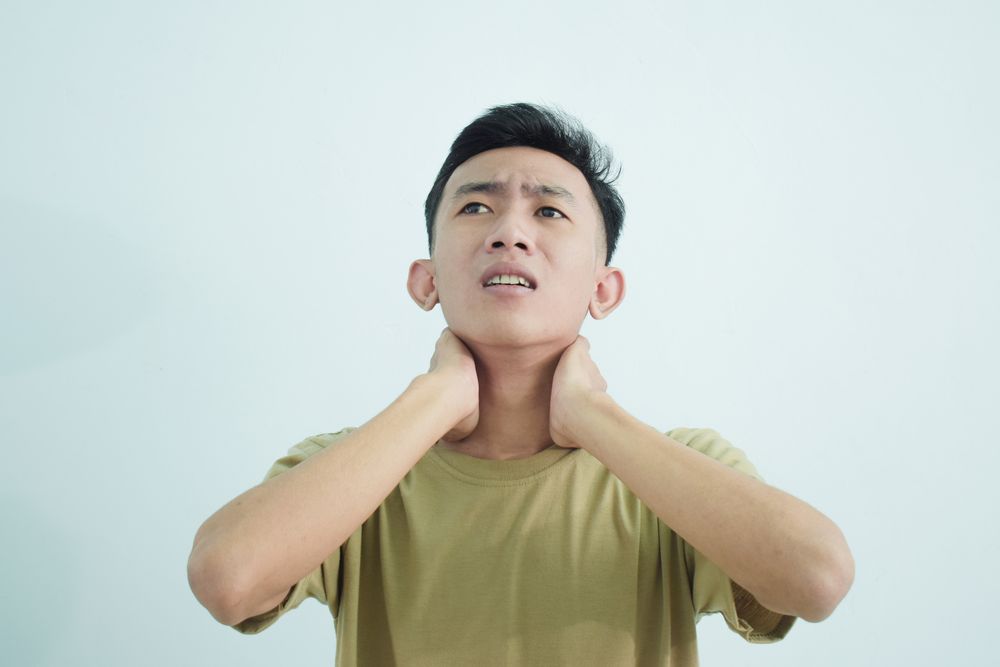 Asian young man touching neck in pain and wincing