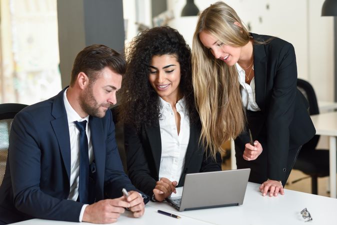 Business co-workers together in office around a laptop