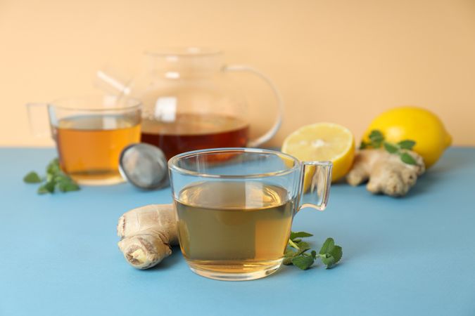 Cups and teapot with tea, lemon, ginger on blue table on beige background