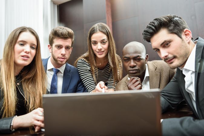 Male and female co-workers gathered around a laptop