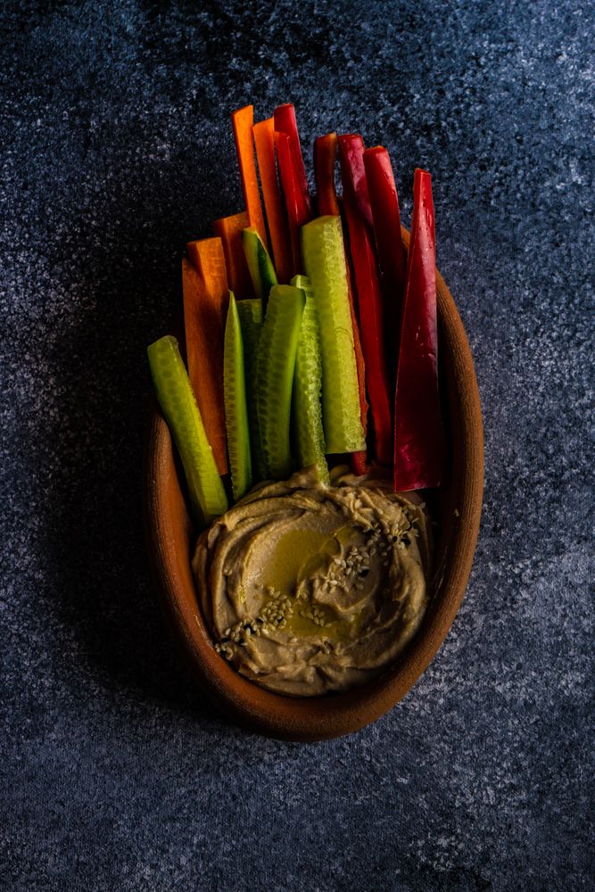 Top view of hummus dish served with chopped veggies on grey counter
