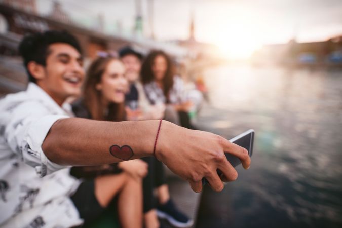 Group of people taking selfie with smart phone with focus on hand