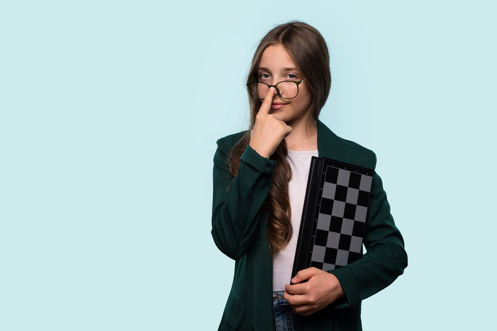 Teen girl holding chessboard, adjusting glasses
