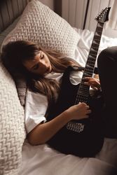 Young brunette woman playing guitar on bed